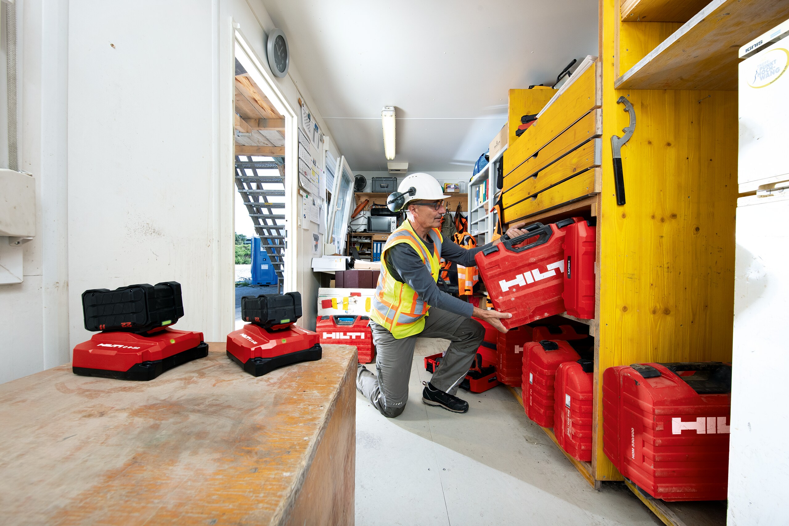 Un  magasinier range un coffret Hilti sur une étagère dans un container de chantier