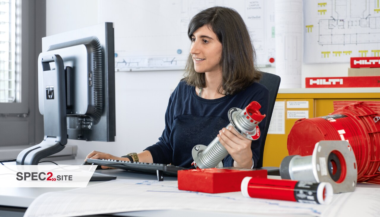 un ingénieur de terrain Hilti montre à un client un manchon coupe-feu dans une application électrique un ingénieur tient une solution coupe-feu tout en regardant un écran d'ordinateur